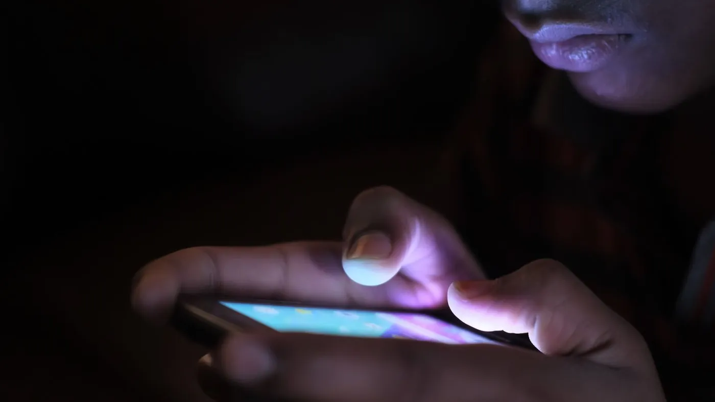 A person holding an illuminated smartphone in the dark, screen glowing.