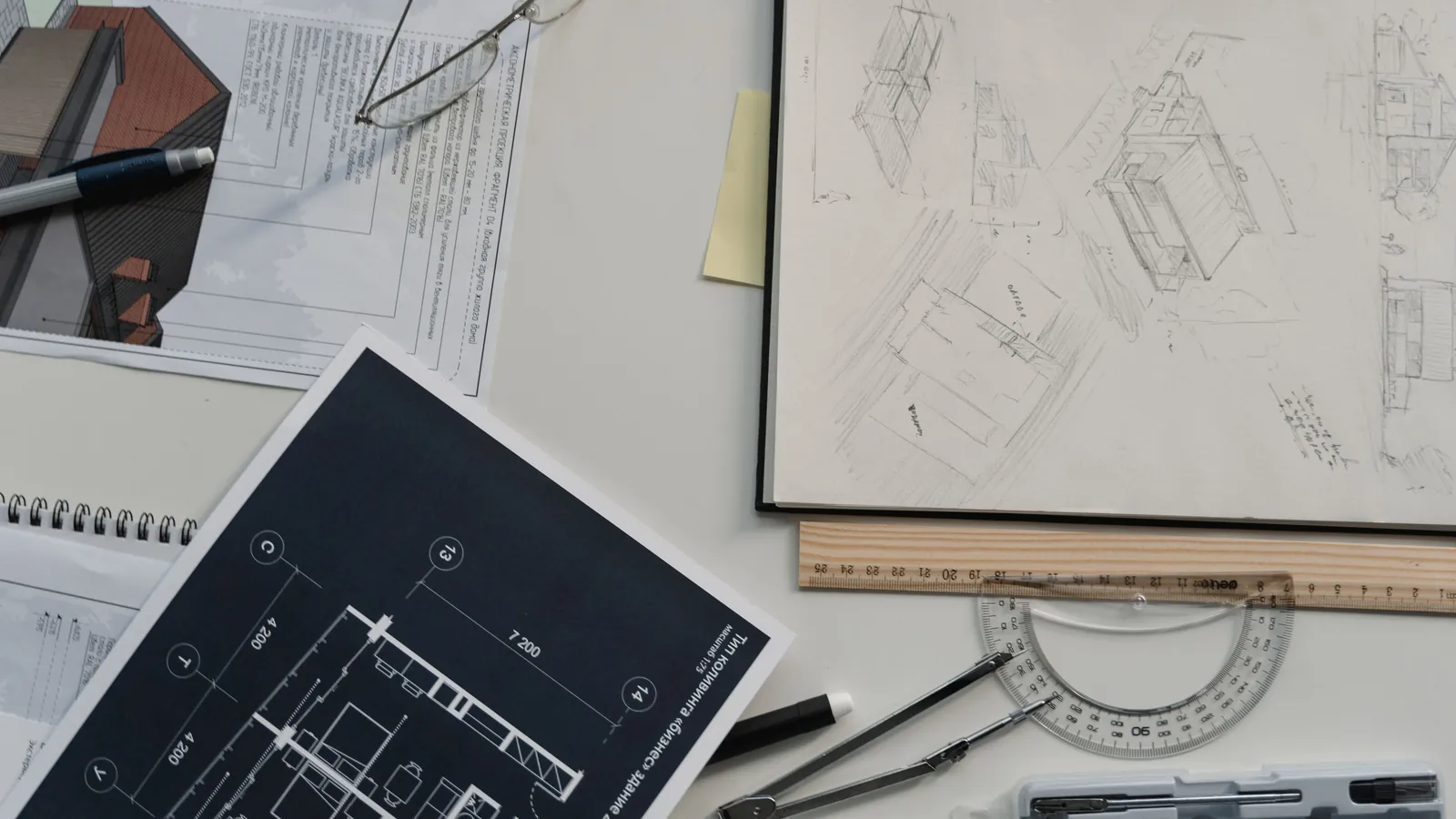 An architect's desk covered with printed floor plans, a navy blueprint, pencil sketches, a wooden ruler, a compass and reading glasses.